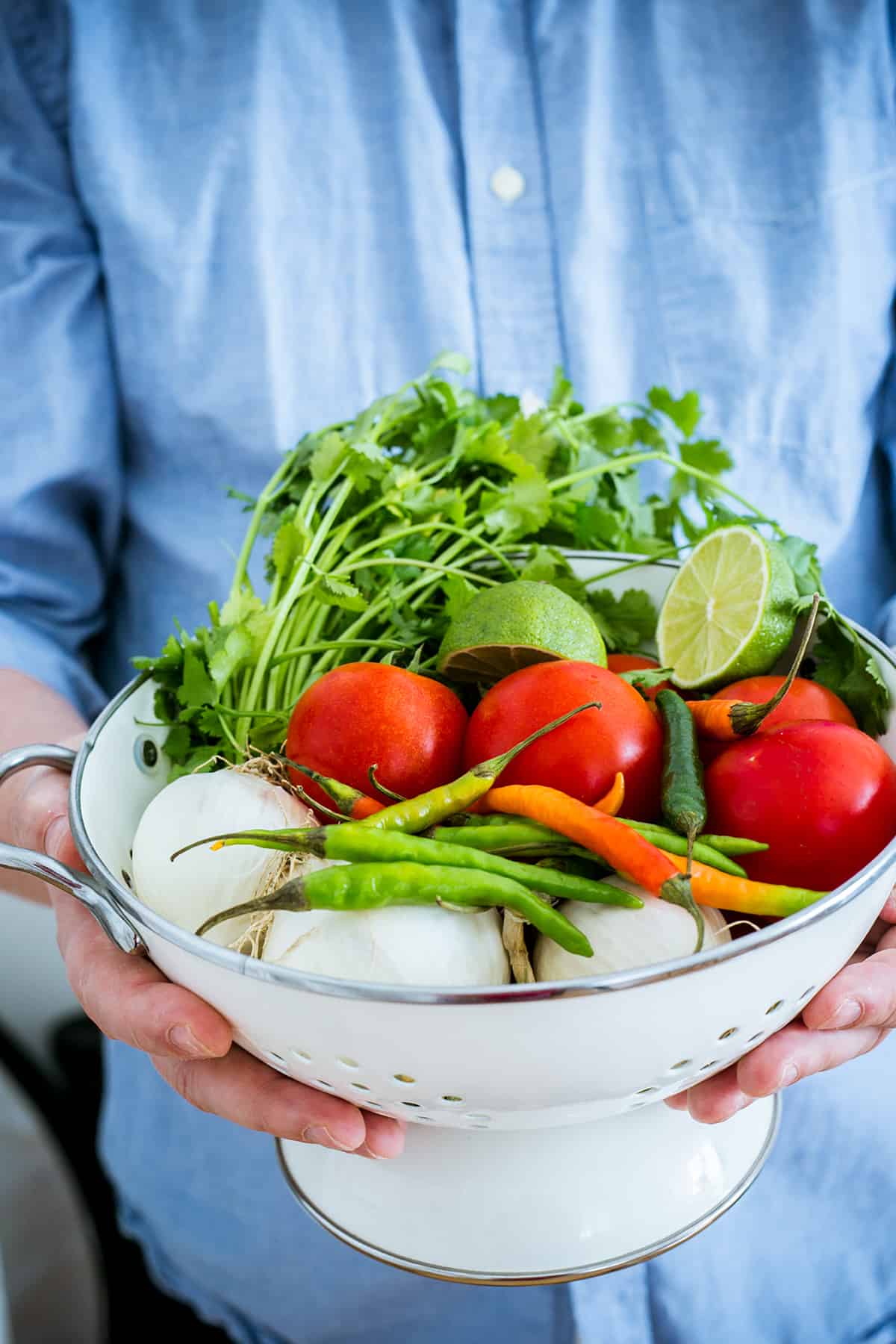 Ingredientes para la salsa de molcajete en un colador que sostiene un hombre.