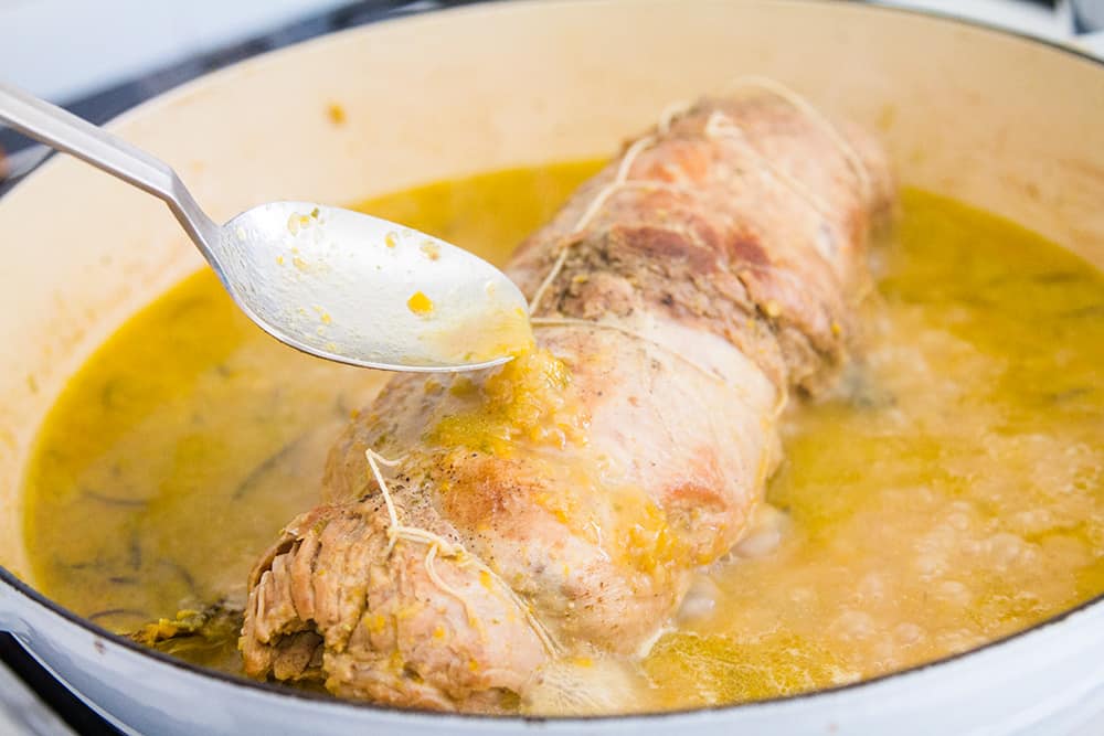 Roast veal being bath with the meat juices on the pan.