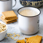 Oatmeal atole de avena on mugs with a Mexican pitcher in the background and some cookies scattered around.