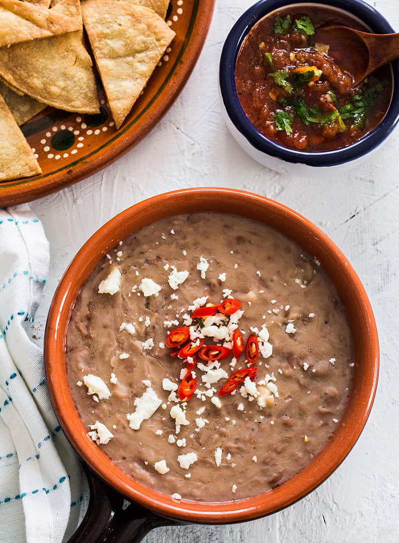 Frijoles fritos en una cazuelita con queso y chiles. Totopos y salsa al lado.