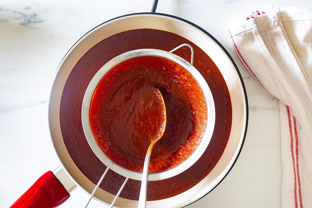 Straining the red enchilada sauce into a pan.