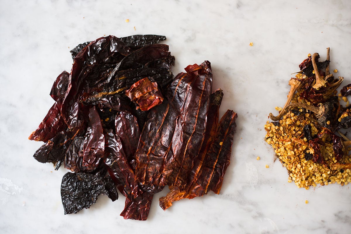 Mexican dried chilies with stems, seeds, and membranes removed on a marble surface.
