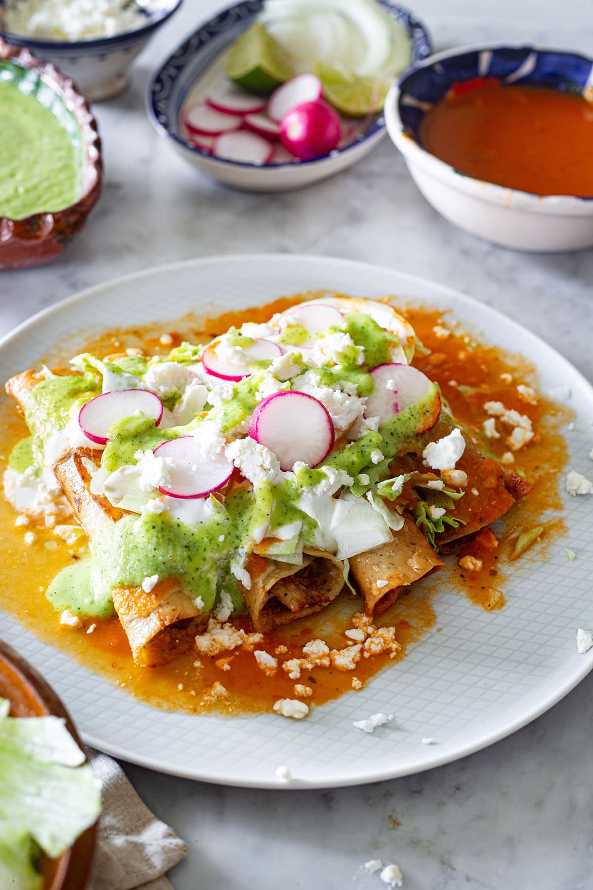 Flautas de pollo Mexicanas servidas con lechuga, cebolla, rabanitos, crema, queso y salsas.