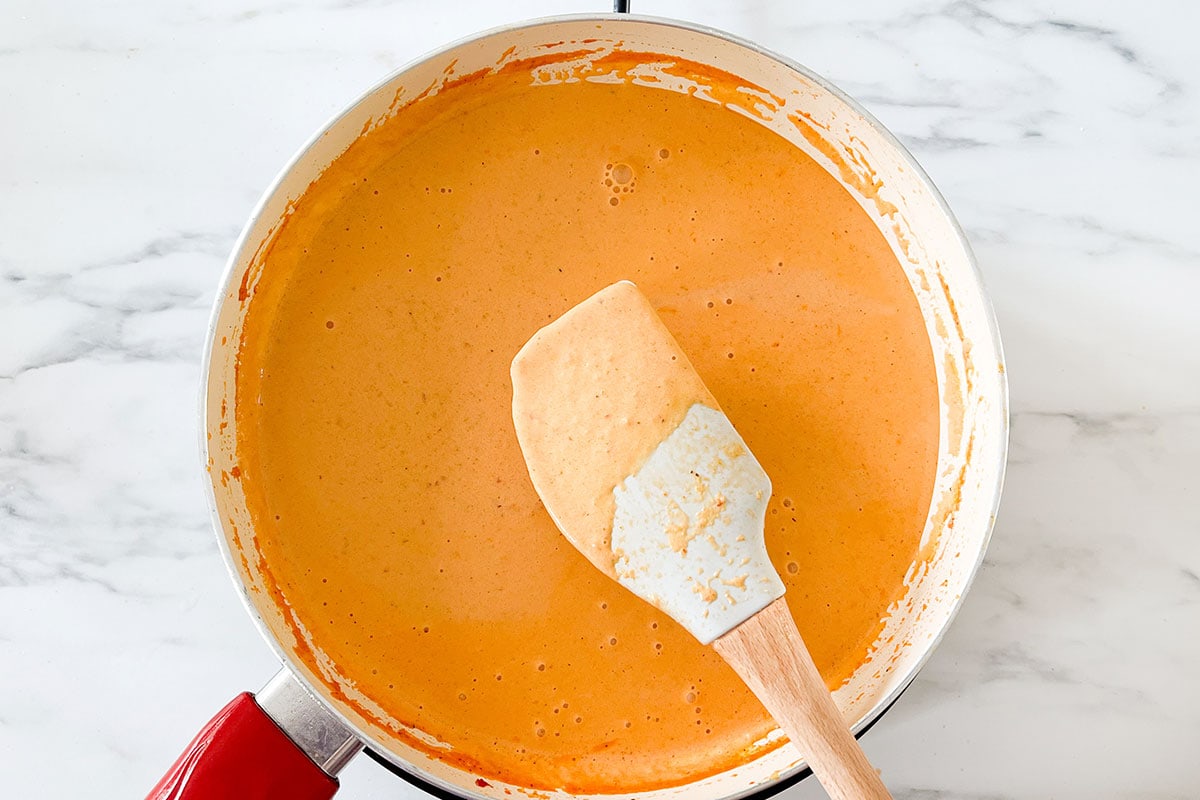 Showing the creamy enchiladas suizas rojas sauce with a spatula.