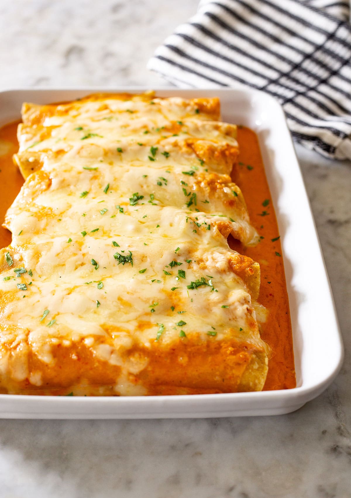 Enchiladas Suizas Rojas in a baking dish on a marble countertop.