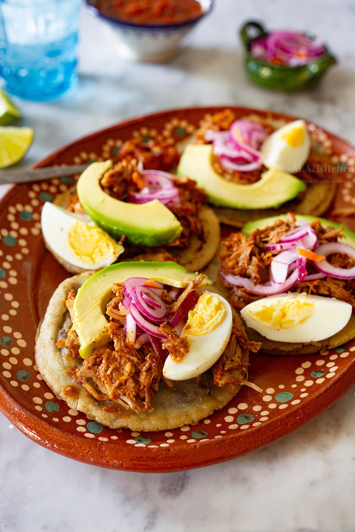Panuchos Yucatecos on a Mexican clay platter with salsa and pickled onions on the side.