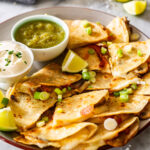 Quesadillas de champiñones on a plate with salsa and sour cream.