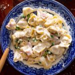 Authentic Italian tortellini alla panna in a plate with a small bowl with parmigiano cheese on the side.