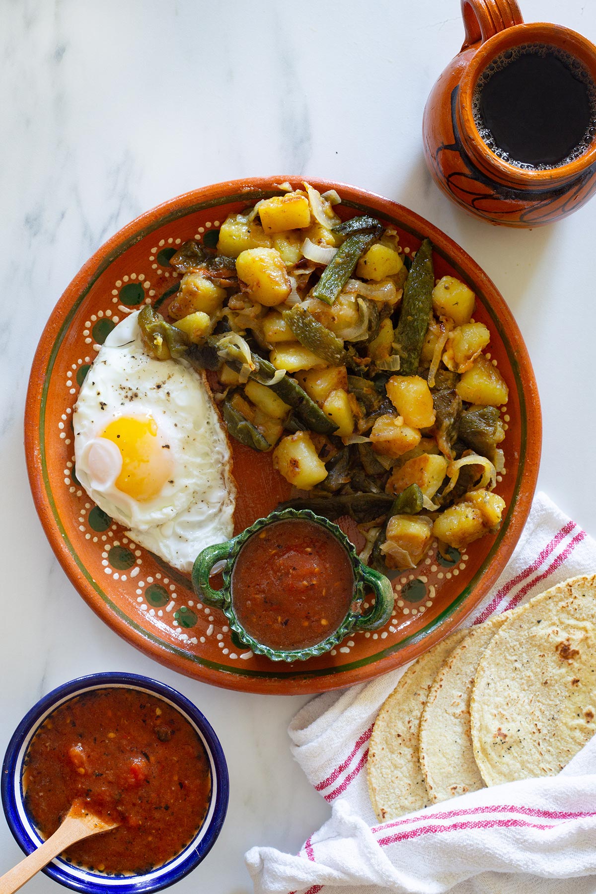 A plate of rajas con papas with a fried egg and salsa on the side, and a mug of coffee.