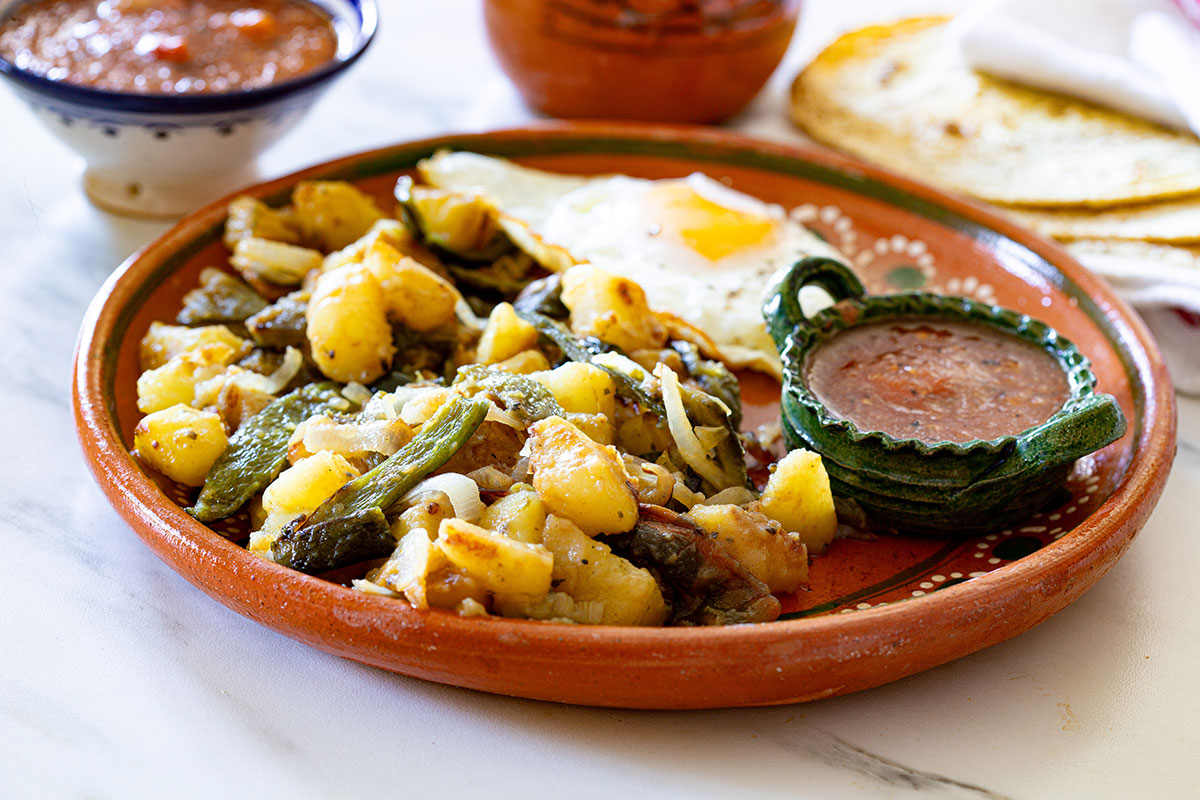 Chile poblano rajas with potatoes in a plate with a small bowl of salsa and a fried egg.